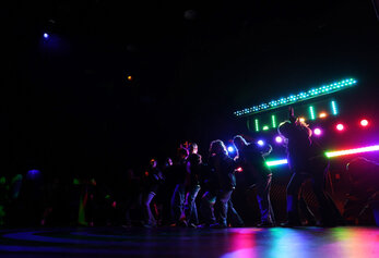 Students perform a choreographed scene in University High School’s “Dreamland,” silhouetted against bright, multicolored stage lights.