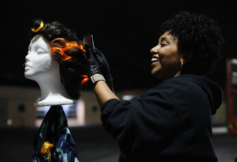A student styles a wig on a mannequin during preparation for University High School’s “Dreamland,” highlighting behind-the-scenes stage tech work.