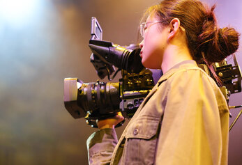 A student operates a camera during a performance in University High School’s “Dreamland,” highlighting stage technology and production work.