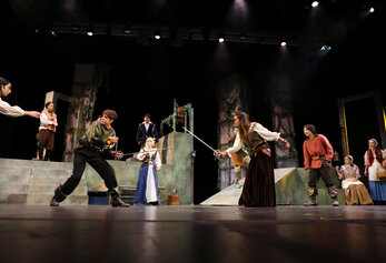 Students perform a sword fight scene in University High School’s “Romeo & Juliet,” surrounded by an ensemble on a multi-level set.